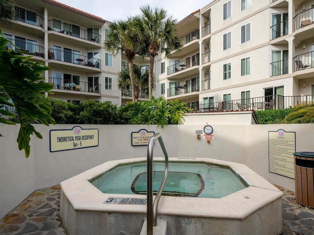 A spa area with a hot tub, a sign indicating a 3% no diving policy, and a building with balconies and palm trees in the background.