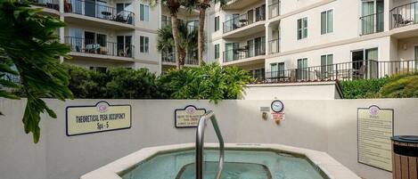 A spa area with a hot tub, a sign indicating a 3% no diving policy, and a building with balconies and palm trees in the background.