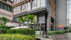 A modern building with a glass facade, outdoor seating area, and greenery. - Seekers Finders Rama IV Hotel, SureStay Collection by BW (Bangkok)