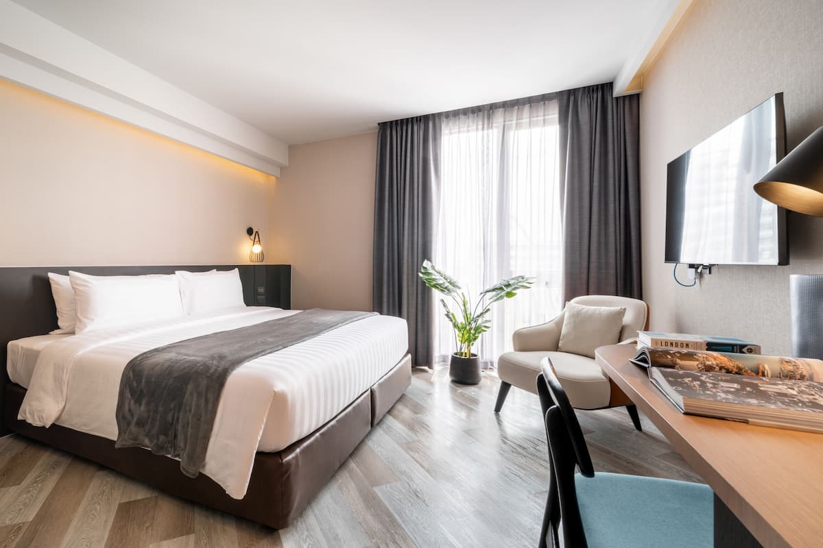 A modern hotel room with a large bed, a desk with a chair, a potted plant, and a TV.