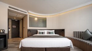 A modern hotel room with a large bed, a built-in desk with a kettle, a seating area with a cushioned bench, and a large mirror on the wall. - Seekers Finders Rama IV Hotel, SureStay Collection by BW (Bangkok)