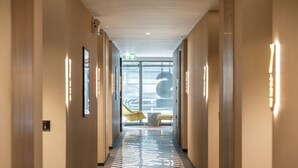 A modern hotel corridor with a central walkway, a yellow chair, and a patterned floor. - Seekers Finders Rama IV Hotel, SureStay Collection by BW (Bangkok)