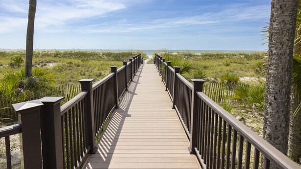 A wooden boardwalk with black railings leading to a beach.