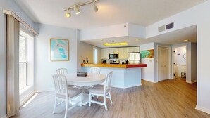 A modern kitchen with white cabinets, a central island, and a dining area with white chairs.