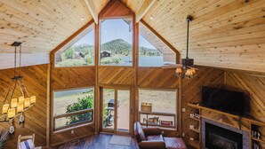 A wooden cabin with a loft bedroom, a fireplace, and large windows offering a view of the outdoors. - On Lake Hatcher. Fish right from home. Hot Tub. (Pagosa Springs)