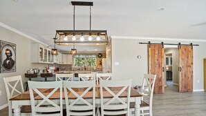 Een moderne keuken met witte kasten, een eethoek met houten stoelen en een grote houten deur.
