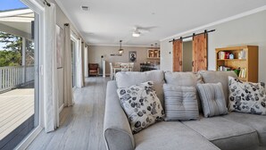 Een ruime woonkamer met een grote grijze bank, een eethoek op de achtergrond, en een kast met een schuifdeur in landhuisstijl.