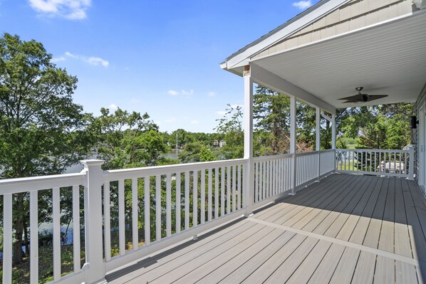 A covered wooden deck with white railings, a ceiling fan, and a view of a lake and trees. - Cozy, waterfront, 5BR 4BA house w 2 decks near USNA & downtown (Annapolis)