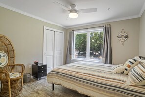 Une chambre à coucher comprenant un lit, une chaise, un ventilateur de plafond, une fenêtre avec des rideaux et un élément de décoration murale.