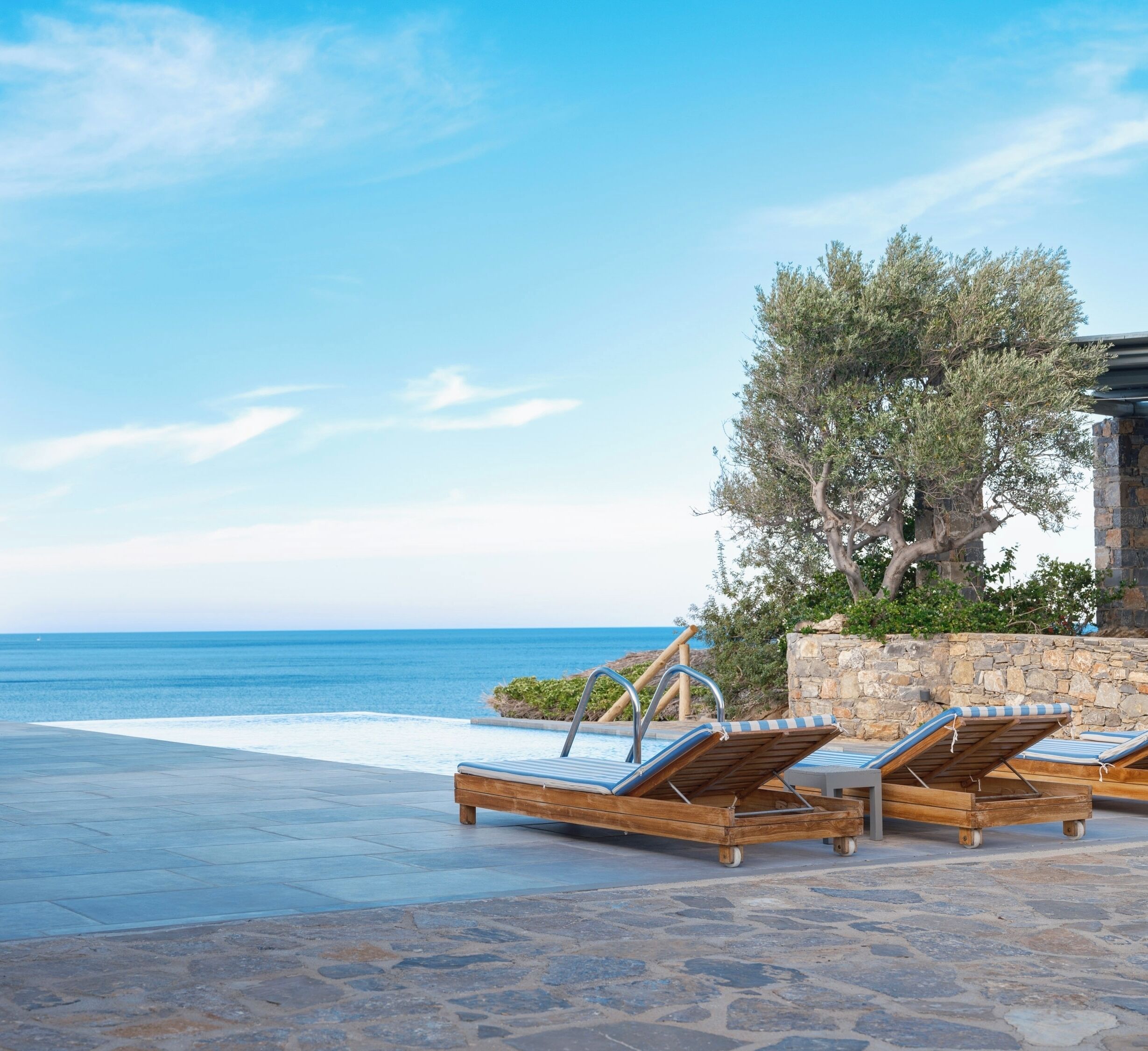 Un espace aménagé au bord de la piscine, avec des chaises longues, un mur en pierre et une vue sur la mer.