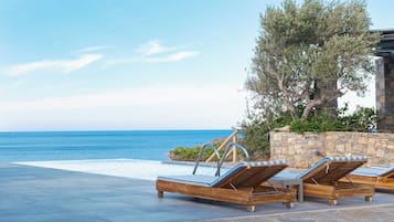 A poolside area with lounge chairs, a stone wall, and a view of the sea.