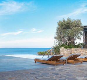 A poolside area with lounge chairs, a stone wall, and a view of the sea.
