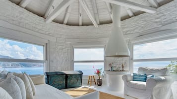 Een ruime kamer met een hoge plafond, grote ramen, een witte bank, een witte fauteuil en een opvallende witte conische lamp.