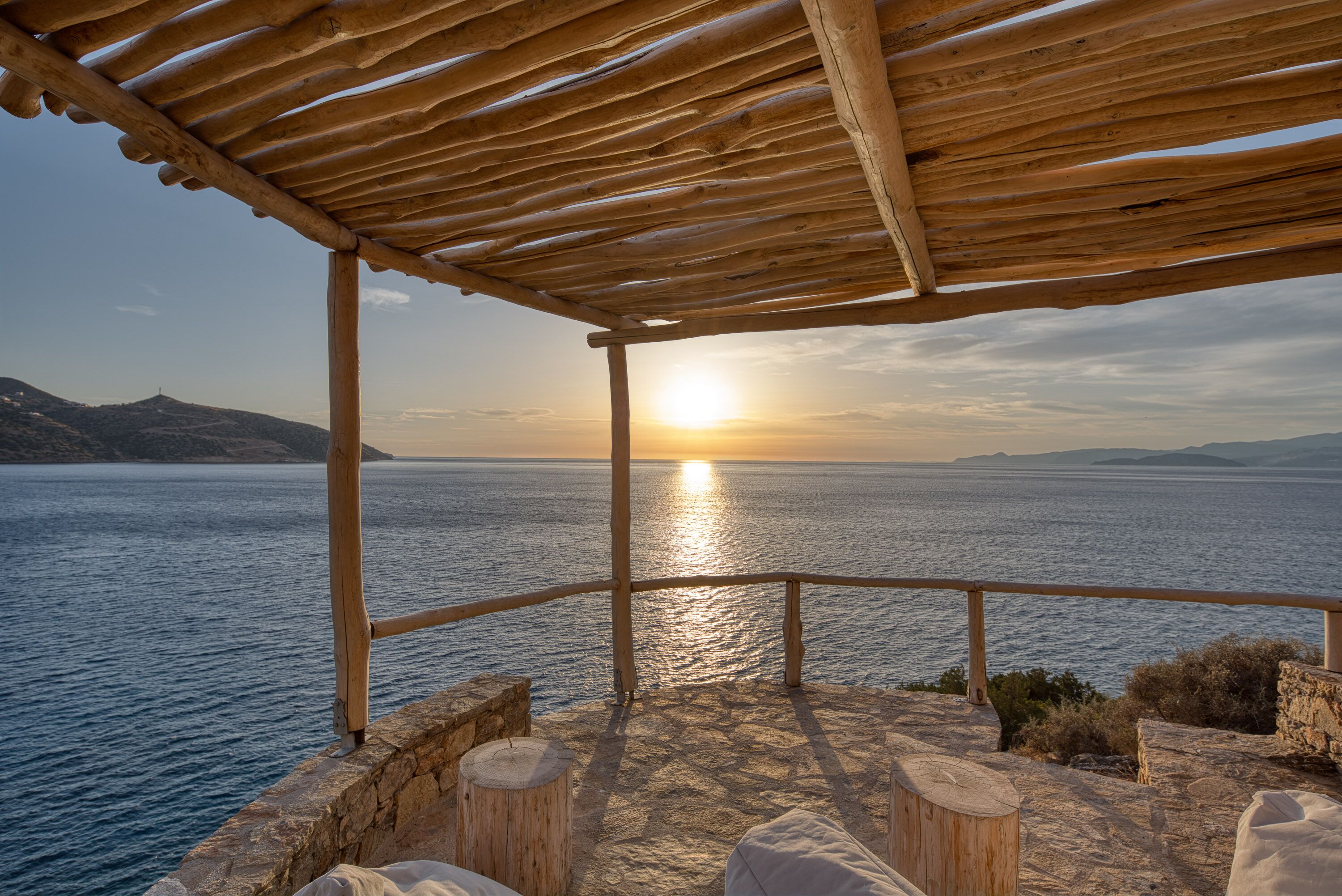 Een houten pergola met uitzicht op een wateroppervlak, de zonsondergang op de achtergrond.