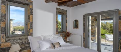 Une chambre avec un lit, une table de chevet, une lampe, un miroir et une vue sur l’extérieur, accessible par une porte vitrée.
