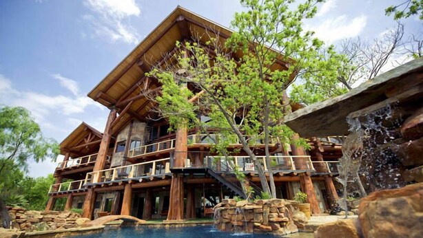 A log cabin-style hotel with a large outdoor pool, a waterfall feature, and a tree in front.