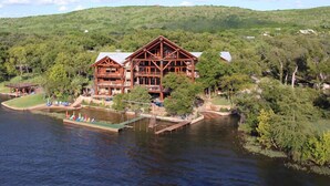 A large wooden lodge with a dock and boats, surrounded by lush greenery and hills.