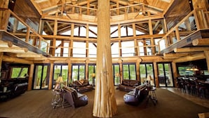 A spacious interior with a high ceiling and a central wooden column, featuring multiple seating areas and large windows.