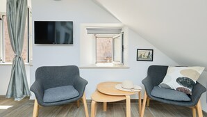Una habitación acogedora con dos sillones grises, una mesita de madera y un televisor montado en la pared.