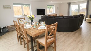 A dining area with a wooden table set for four, a black leather sofa, and a flat-screen TV mounted on the wall. - 3 Praa Cove (Penzance)