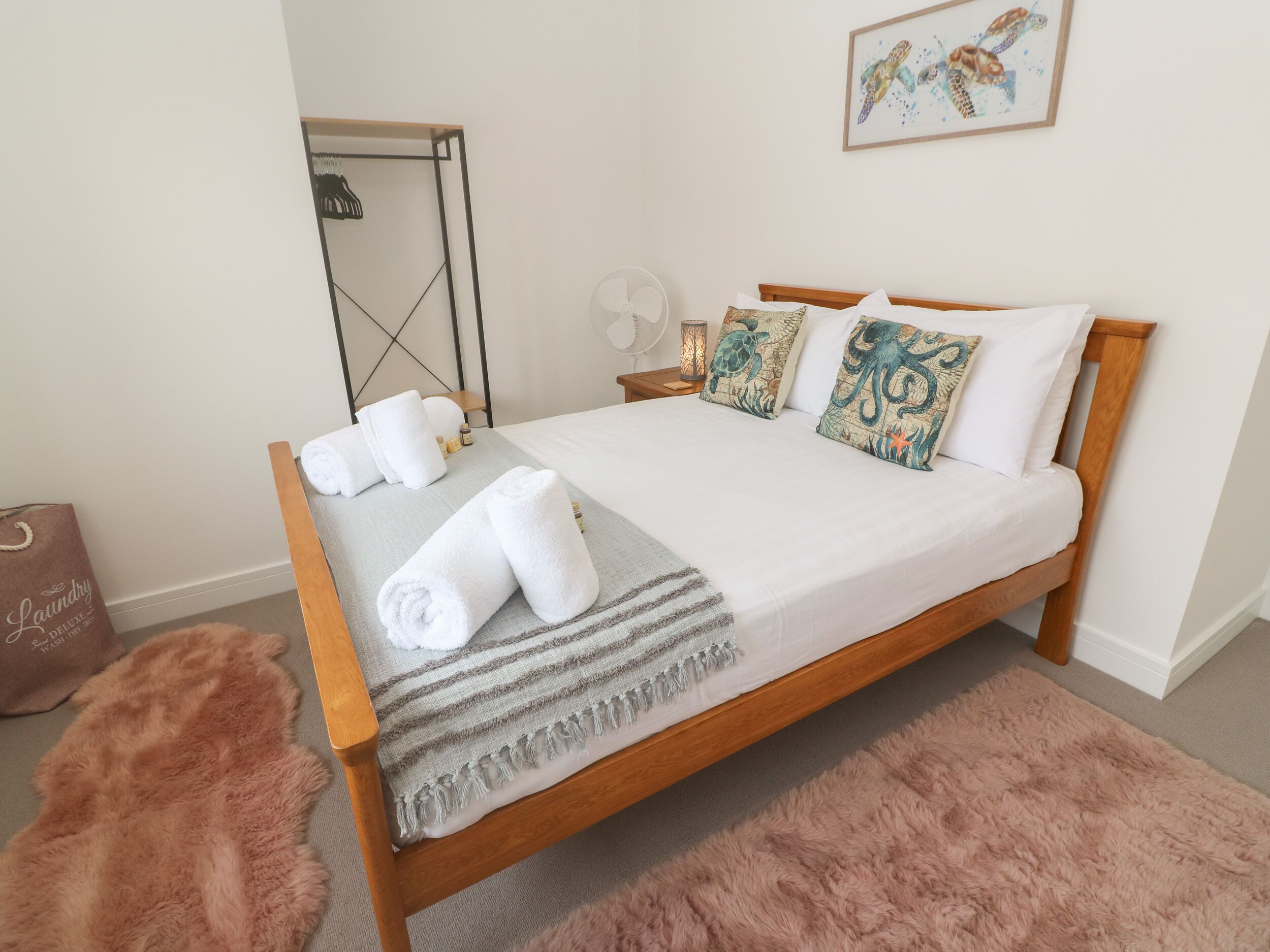A neatly made bed with white linens and decorative pillows, a fluffy rug, and a wooden headboard.