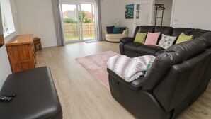 A living room with a leather sofa, a wooden cabinet, a small table, and a sliding glass door leading to a backyard. - 3 Praa Cove (Penzance)