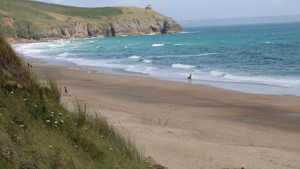 A coastal beach with a grassy cliff and a small building on top. - 3 Praa Cove (Penzance)