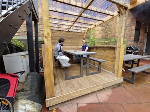 A wooden pergola structure with tables and benches, a grill, and a covered area with a metal roof. - Belford Hostel (Edinburgh)