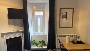 A room with a fireplace, a television, a window with curtains, a dining table with chairs, and a radiator. - Belford Hostel (Edinburgh)