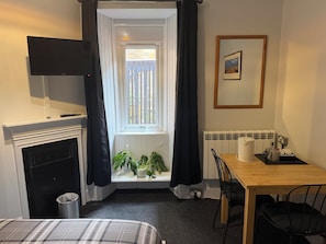 Una habitación con chimenea, televisor, ventana con cortinas, una mesa de comedor con sillas y un radiador.