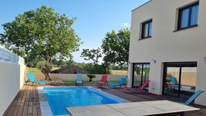 A wooden deck with a pool, lounge chairs, and a table. - La Villa Manon - FLORENSAC (Florensac)