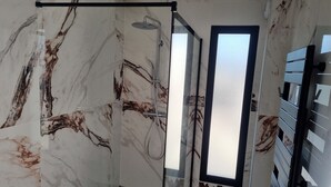 A modern bathroom with a glass-enclosed shower, marble walls, and a wooden floor. - La Villa Manon - FLORENSAC (Florensac)