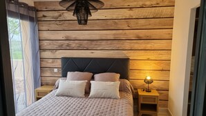 A bedroom with a wooden wall, a bed with a tufted headboard, and a bedside lamp. - La Villa Manon - FLORENSAC (Florensac)