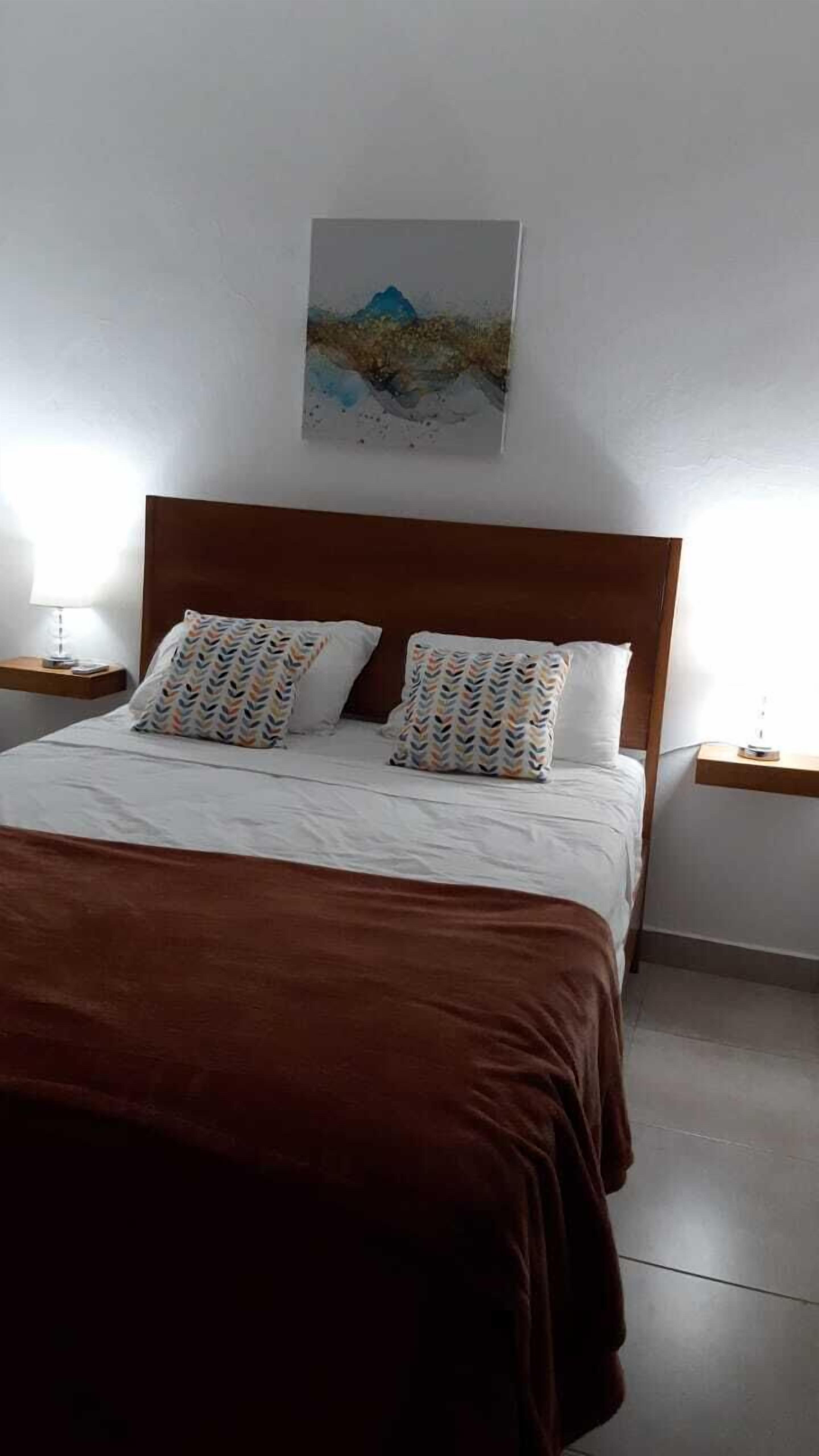 Een netjes opgemaakt bed met gestreepte kussens, een houten hoofdbord en een schilderij aan de muur.
