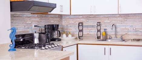 A modern kitchen with white cabinets, a gas stove, a coffee maker, and a sink.