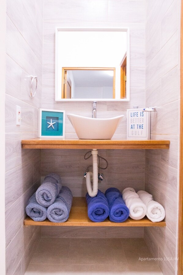 Un baño con lavamanos, espejo y perchero. Hay un letrero que dice "Life is better at the Gulf".