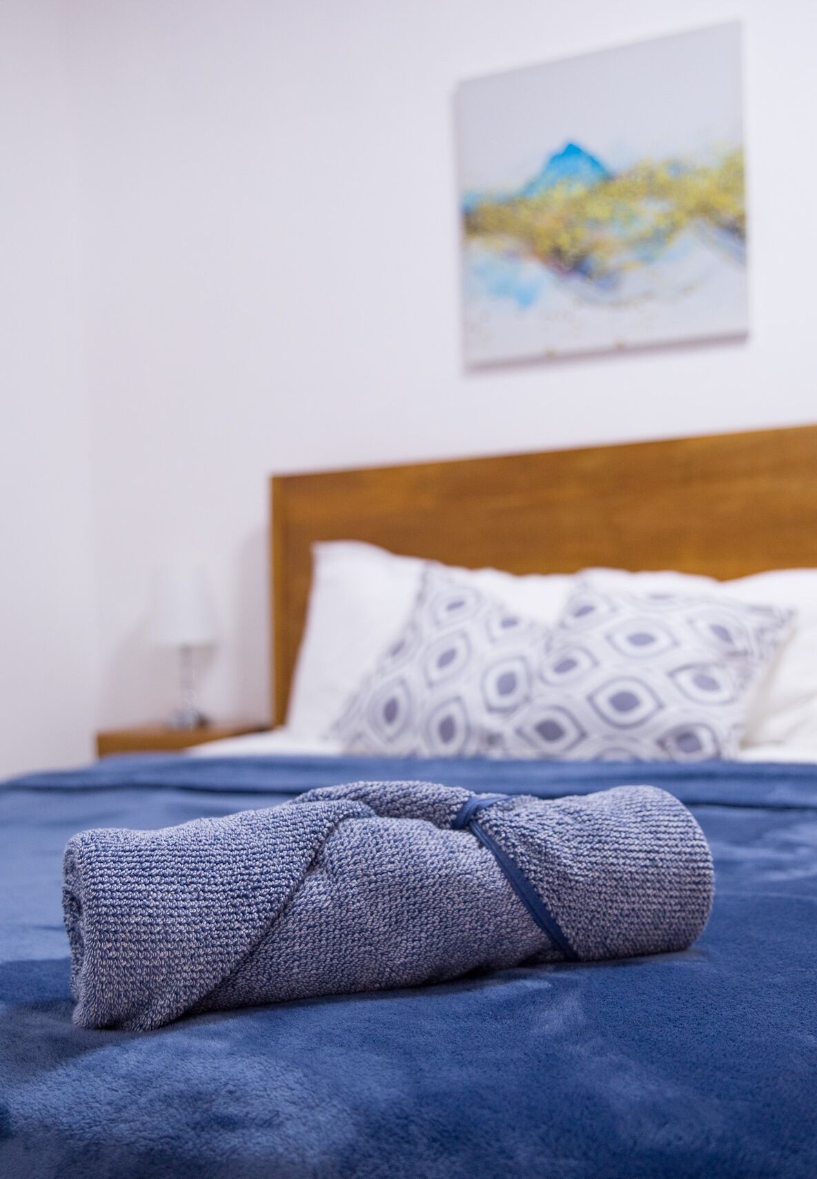 A neatly made bed with a blue blanket and a rolled-up towel on a blue bedspread.