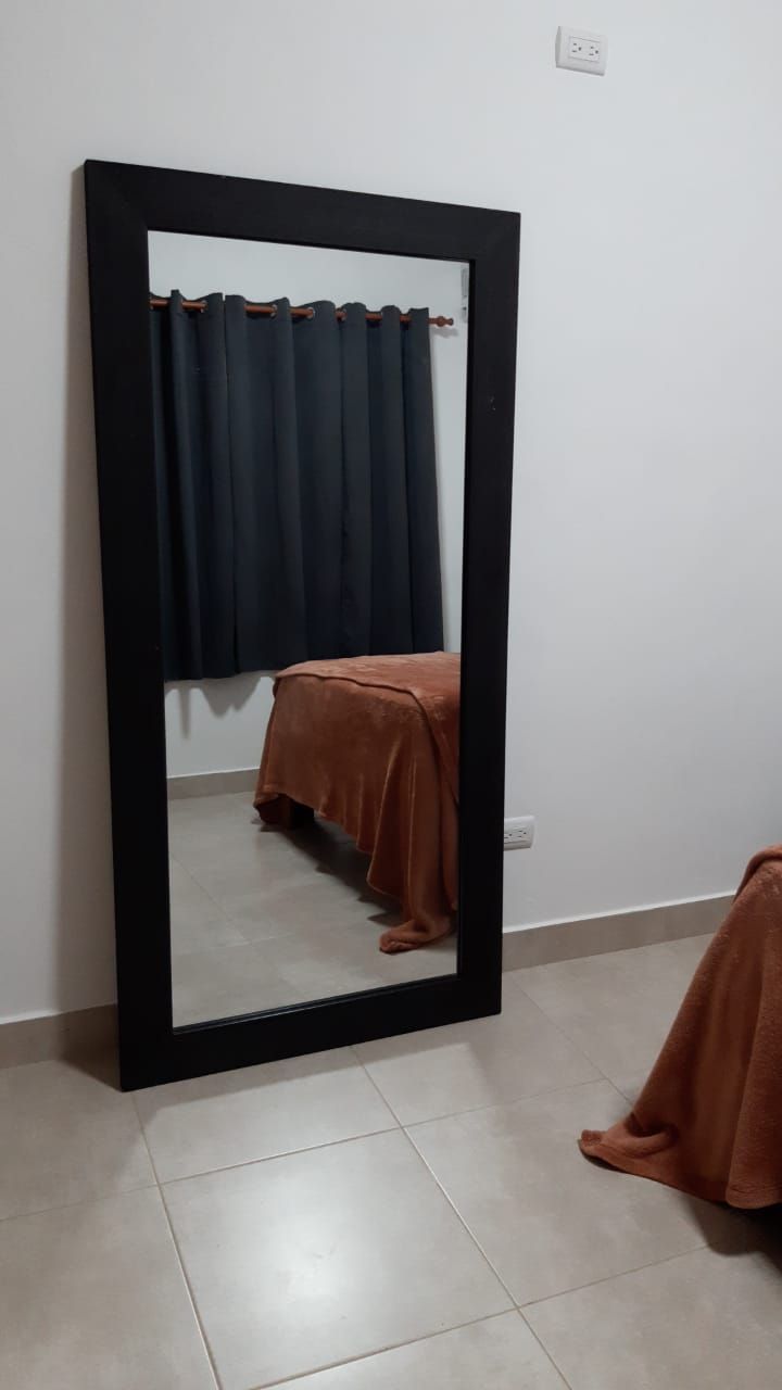 A room with a large mirror, a bed with a brown cover, and a curtain.