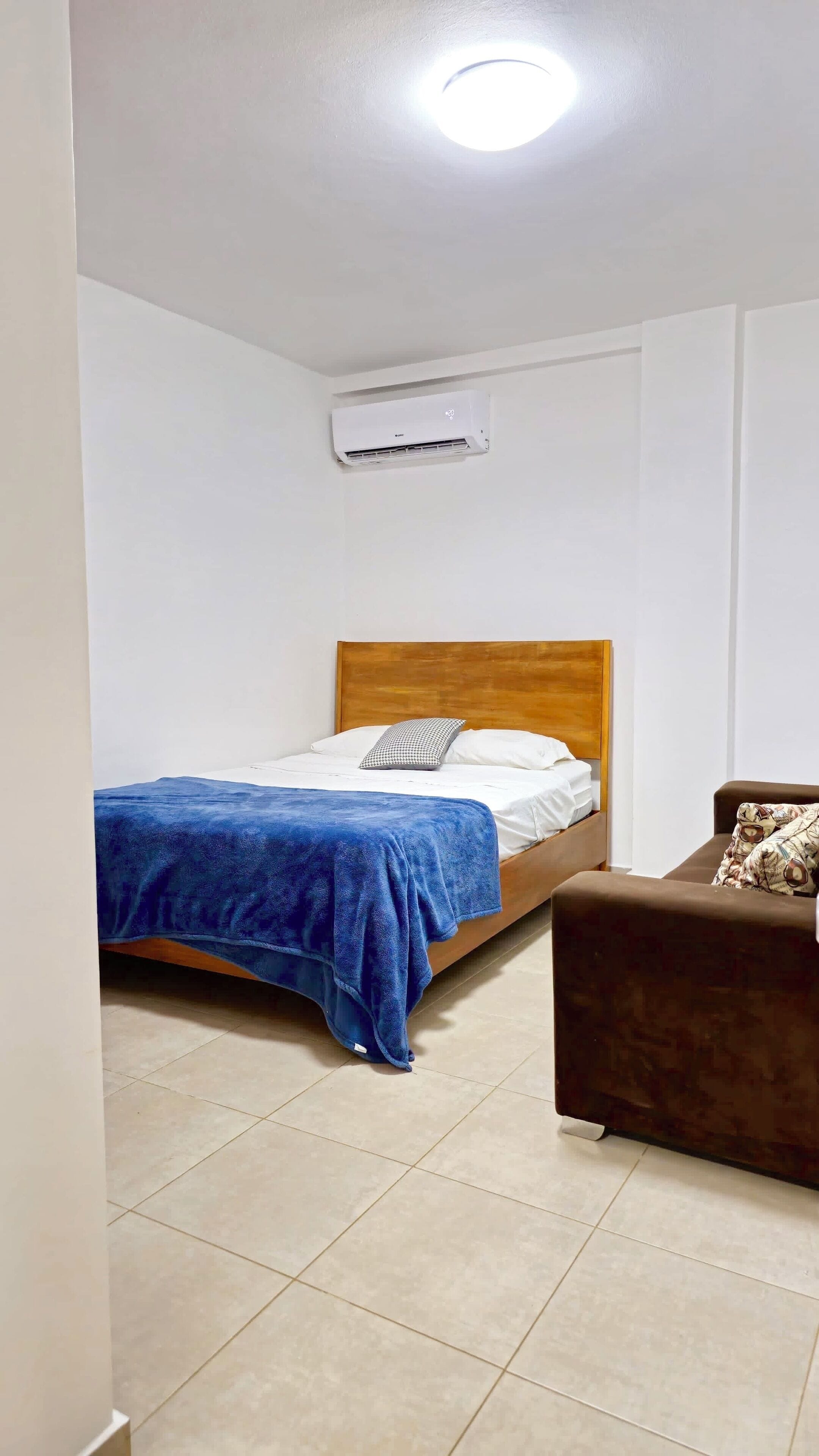 Une chambre à coucher avec un lit, un canapé marron et un appareil de climatisation fixé au mur.