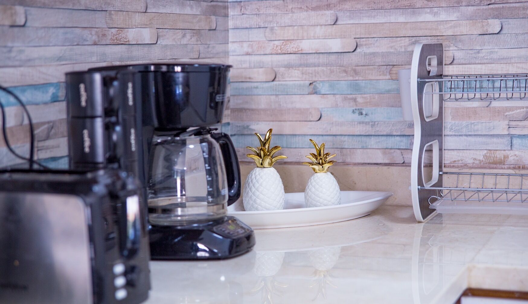 Une cuisine équipée d’une machine à café, de deux vases décoratifs en forme d’ananas et d’une étagère en métal.