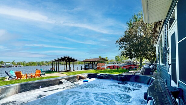 A hot tub area with lounge chairs and a gazebo by a lake.