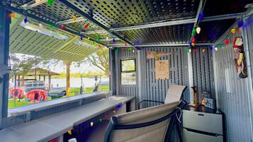 A compact, metal-framed room with a bench, a small table, and a refrigerator. There are colorful string lights and a sign on the wall.