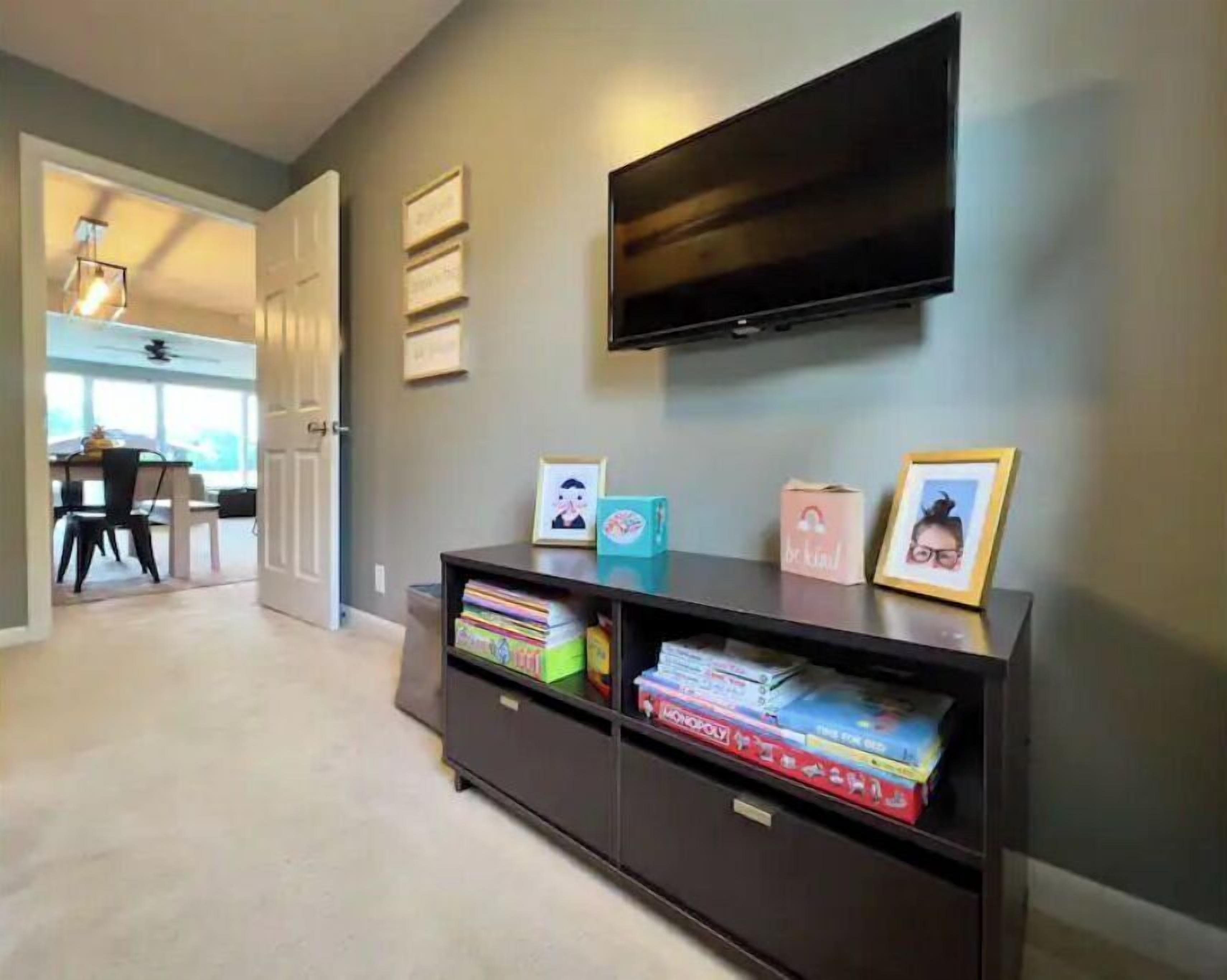 A hallway with a dark-colored console table holding board games and framed pictures. A flat-screen TV is mounted on the wall above the table.