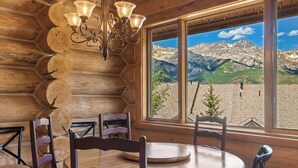 Un interior de madera con una mesa redonda y sillas, una lámpara de araña y un ventanal con vistas a la montaña.