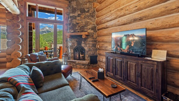 Interior de una cabaña de troncos con chimenea de piedra, televisor y una zona de estar acogedora.