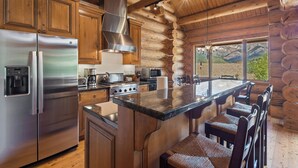 Una cocina moderna con una isla grande, electrodomésticos de acero inoxidable, armarios de madera y vistas a montañas a través de las ventanas.