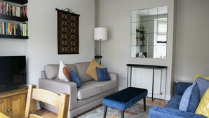Een woonkamer met een bank, een salontafel, een televisie, een boekenkast en een kamerbreed tapijt met een patroon.