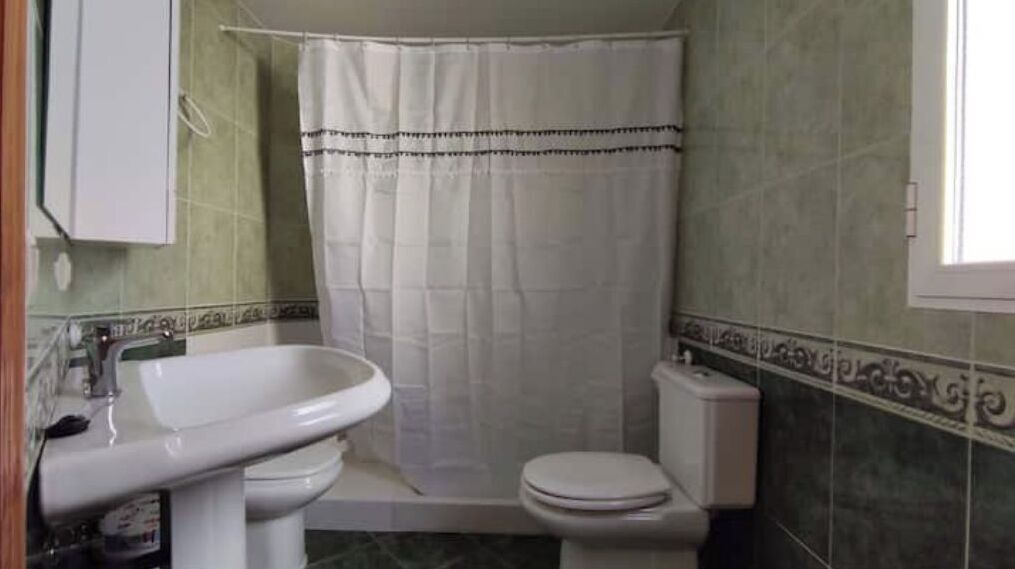 Et badeværelse med vask, toilet og bruseforhæng.