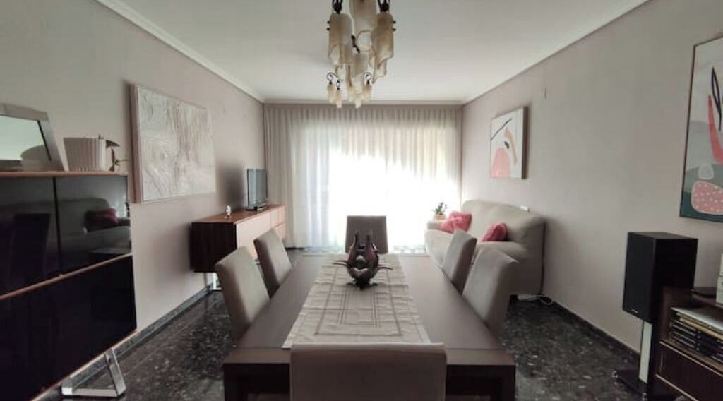 A modern hotel room with a dining table, sofa, and TV.