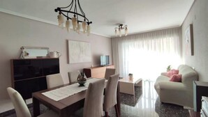 A modern living room with a dining area, a sofa, a TV, and a chandelier. - Avenue viewpoint (Albaida)